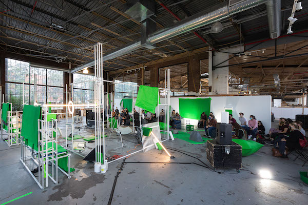 Bright green fabric hanging from white frames with a group of people seated in the background