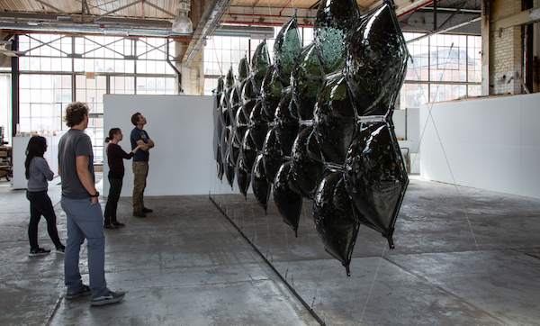 People looking at a glass slumping sculpture suspended from the ceiling