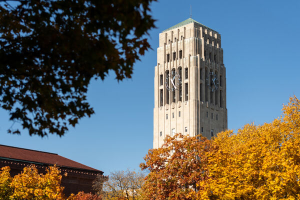 The top of Burton Memorial Tower on a fall day with a tree's yellow leaves in front of it