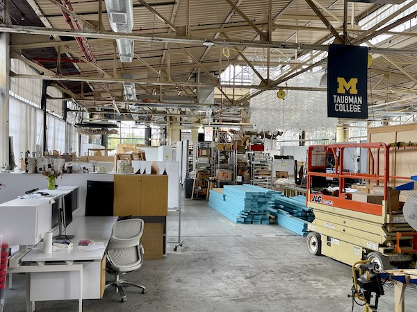 The warehouse-like interior of the Annex filled with project materials and a block M flag hanging from the rafters