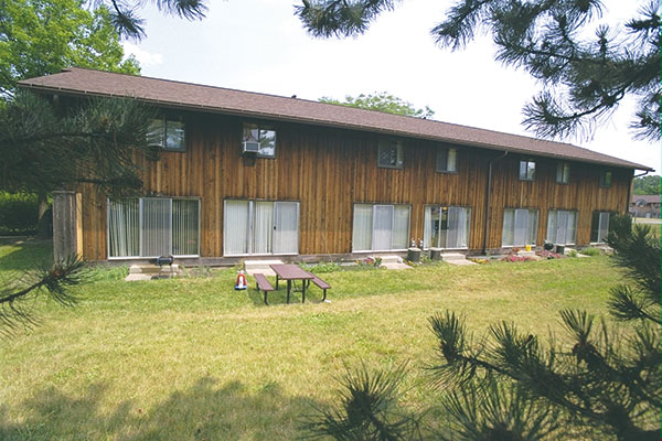 The rear of a two-story wooden apartment building with a field of grass and picnic tables
