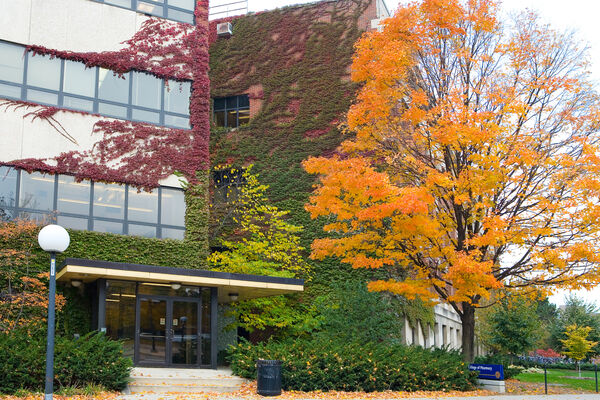 The exterior of the College of Pharmacy in the fall with a tree with bright orange leaves