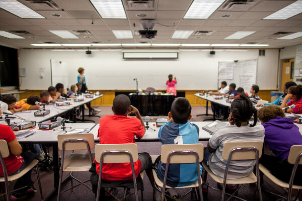 Students sitting in class at tables in a u-shaped formation while an instructor writes on a whiteboard