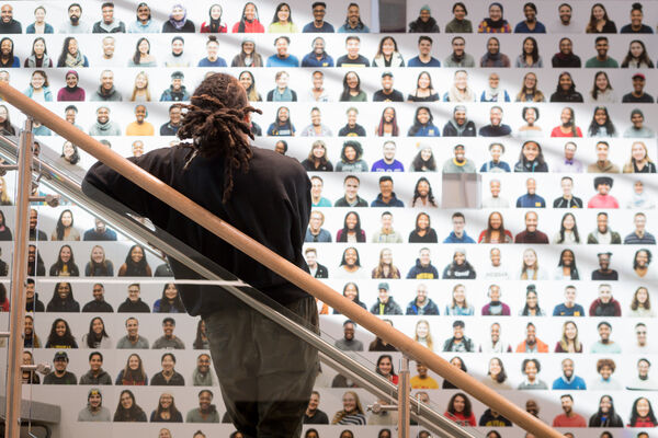 A person standing on a stairwell at the Trotter Multicultural Center looking at a mosaic of people's faces on the wall